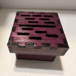 A deep purple wood box with randomly placed rectangular slots on top of the lid